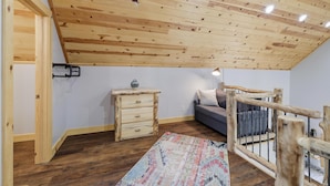 Ett sovrum i loftstil med ett sluttande tak, synliga träbjälkar, en soffa, en byrå och en mönstrad matta.