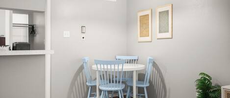 Un comedor con una mesa redonda y cuatro sillas azules, una lámpara colgante blanca y dos cuadros en la pared.