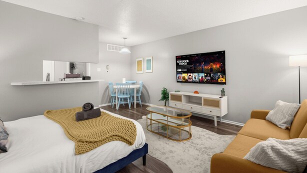 A modern living room with a bed, a sofa, a dining area, and a TV mounted on the wall. - Modern Central Austin Retreat Near UT & Downtown (Austin)