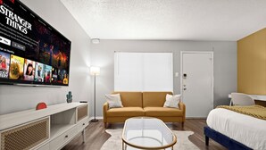 A modern bedroom with a sofa, a bed, a TV mounted on the wall, and a small table. - Modern Central Austin Retreat Near UT & Downtown (Austin)