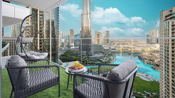 Un balcon avec des fauteuils en osier, une table à manger ornée de fruits et une vue sur le paysage urbain, avec notamment un grand gratte-ciel.