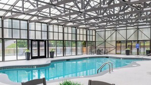Uma piscina interior com paredes de vidro transparente, mesa de bilhar e cadeiras.