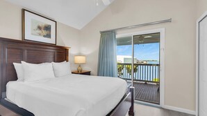 A hotel room with a large bed, a nightstand with a lamp, a framed picture on the wall, and a balcony with a view of the water. - Duck Key Townhome on open Water (Duck Key)
