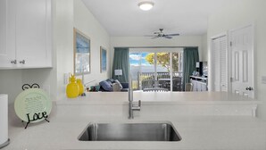 A modern kitchen with a stainless steel sink, a dining area with a table and chairs, a ceiling fan, and a view of the outdoors. - Duck Key Townhome on open Water (Duck Key)
