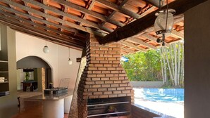 Ein Außenbereich mit Küche, der ein Backofen aus Ziegeln, eine Betonarbeitsplatte und einen Blick auf einen Swimmingpool bietet.