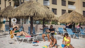 A beach with thatched umbrellas, lounge chairs, and a pool area. - Last minute deal on Aruba Resort;Large 1st Floor Suite;Sleeps 4; 1 MasterBedroom (Oranjestad)