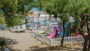 Ein Spielplatz am Strand mit Schaukeln, Rutschen und einem eingezäunten Bereich.