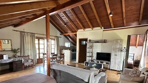 Ein geräumiges Schlafzimmer im Loft-Stil mit hoher Decke und freiliegenden Holzbalken, ausgestattet mit zwei großen Betten und einer gemütlichen Sitzecke mit Kamin.