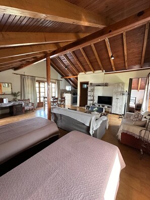 Amplio dormitorio tipo loft con techo alto y vigas de madera a la vista, que cuenta con dos camas grandes y una zona de estar acogedora con chimenea.