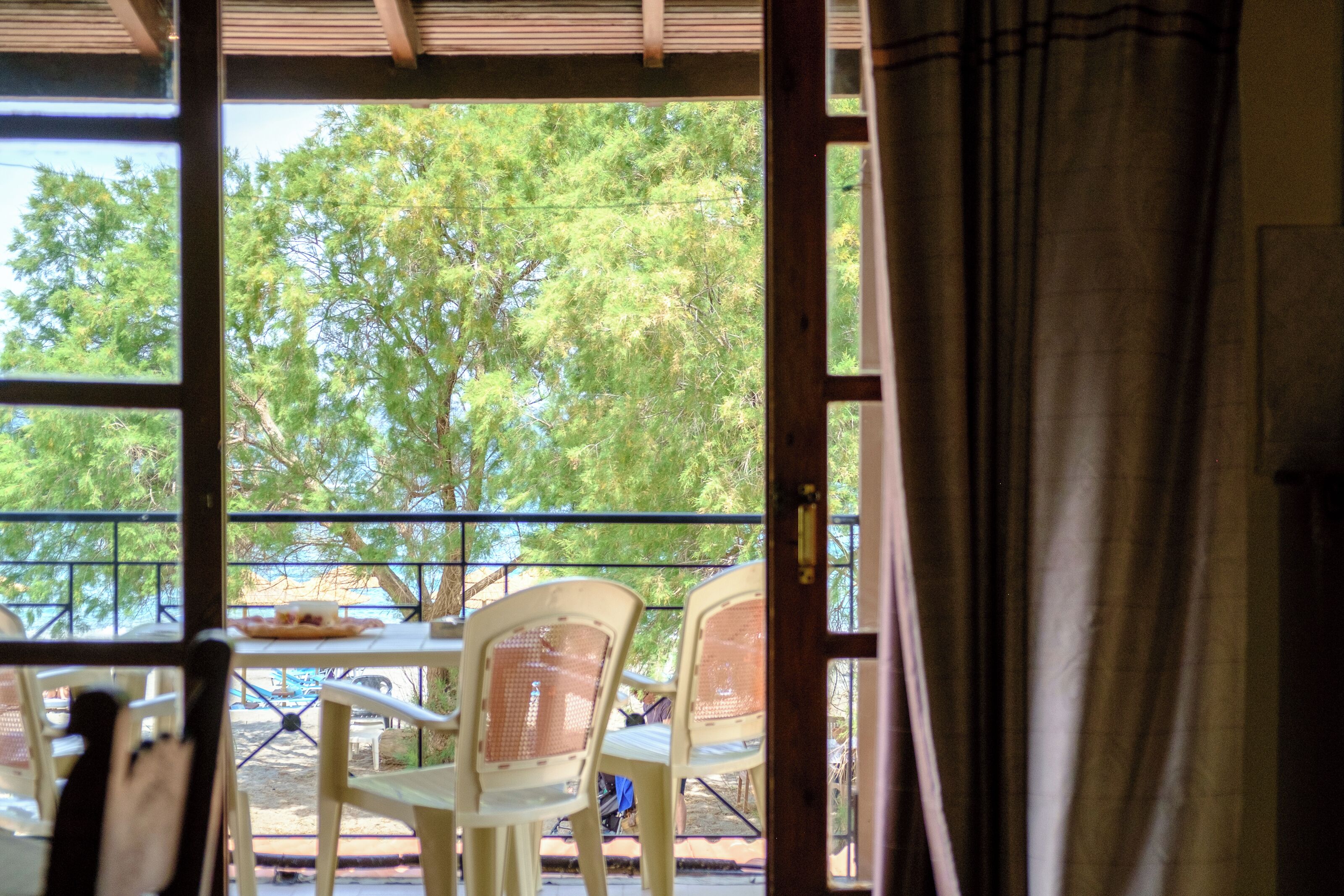 An outdoor seating area with a table and chairs, a view of trees through a window, and a curtain partially covering the window.