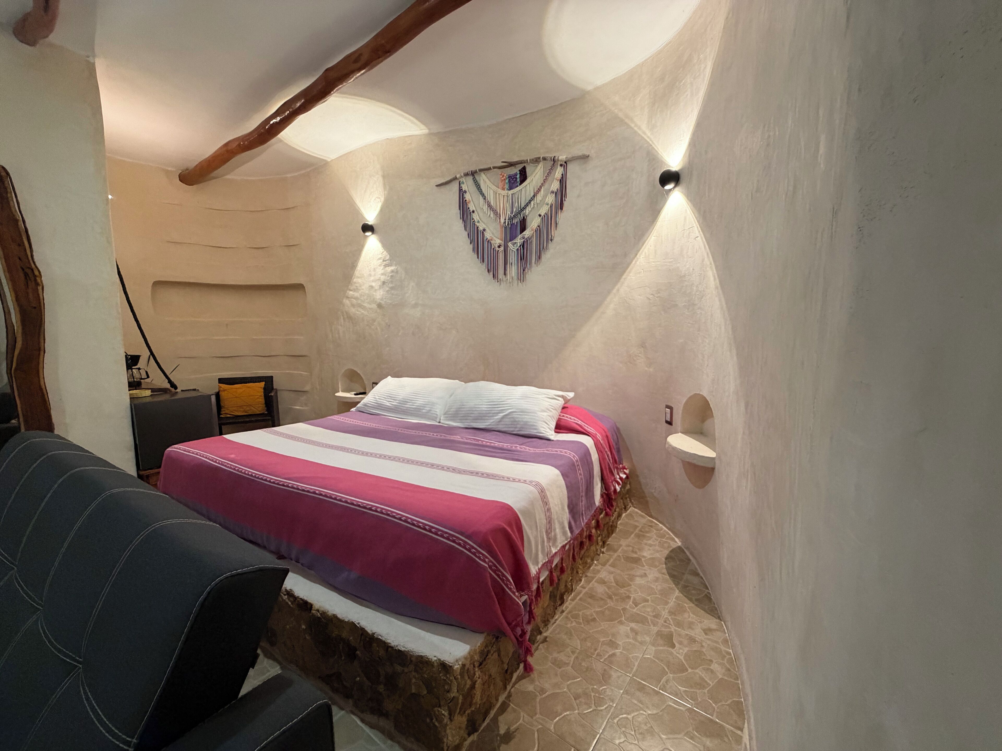 Ein Schlafzimmer mit einem Bett, einem Sessel, einem Nachttisch und einem an der Wand befestigten Regal.