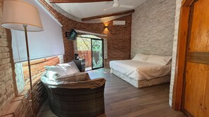 A cozy room with a bed, a wicker chair, a lamp, and a large window with a view of greenery.