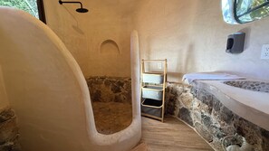 A bathroom with a stone wall, a bathtub, a shower, and a wooden shelf.