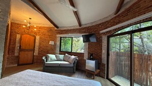 A cozy room with a bed, a sofa, a TV, and a window with a view of trees. - Finca Oz (Homún)