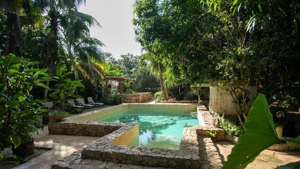A pool surrounded by stone walls and lush greenery, with a stone pathway leading to it. - Finca Oz (Homún)