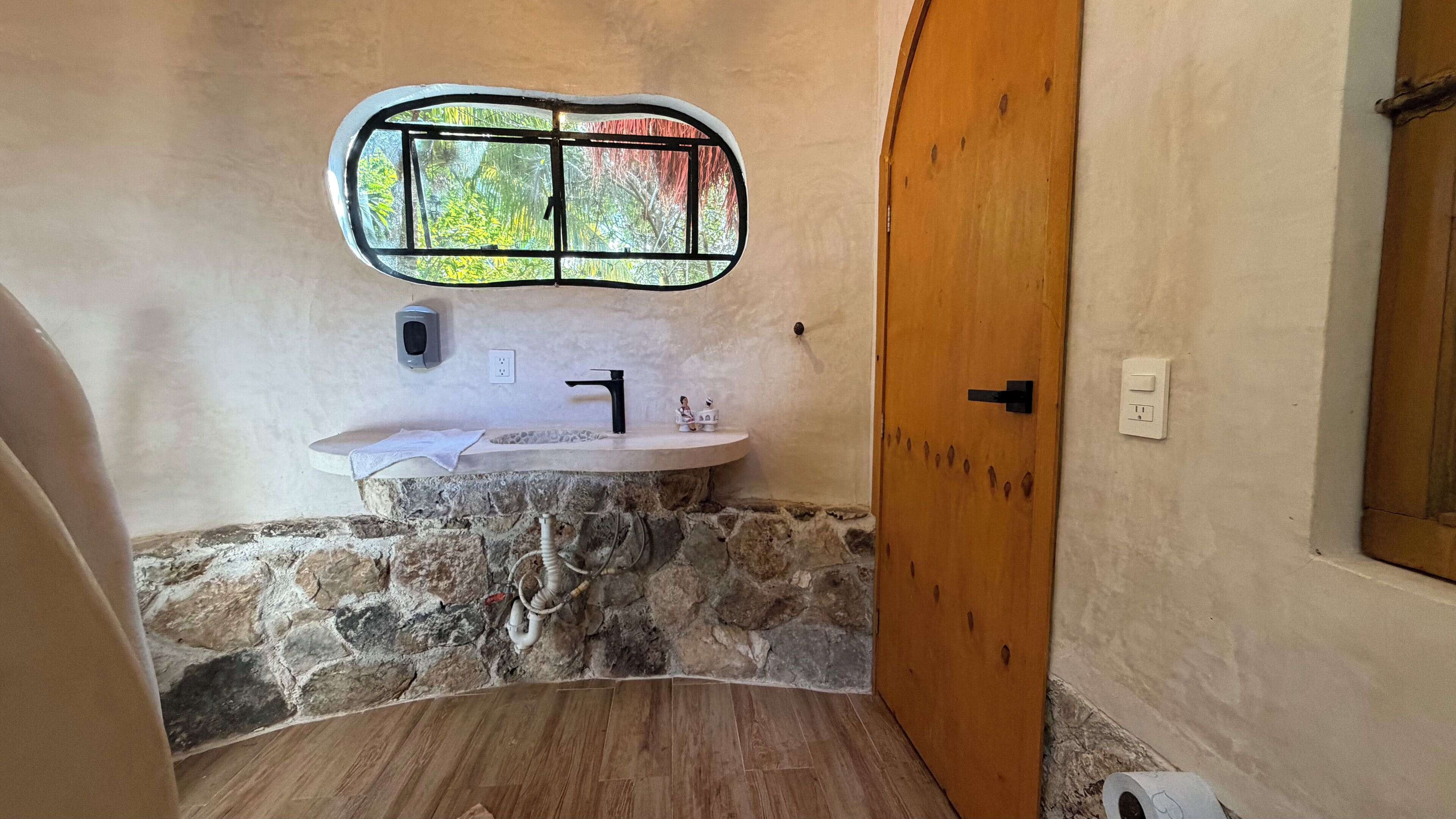 A bathroom with a stone sink, a window with a view of trees, and a wooden door.