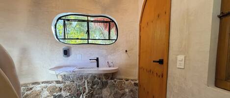 A bathroom with a stone sink, a window with a view of trees, and a wooden door.