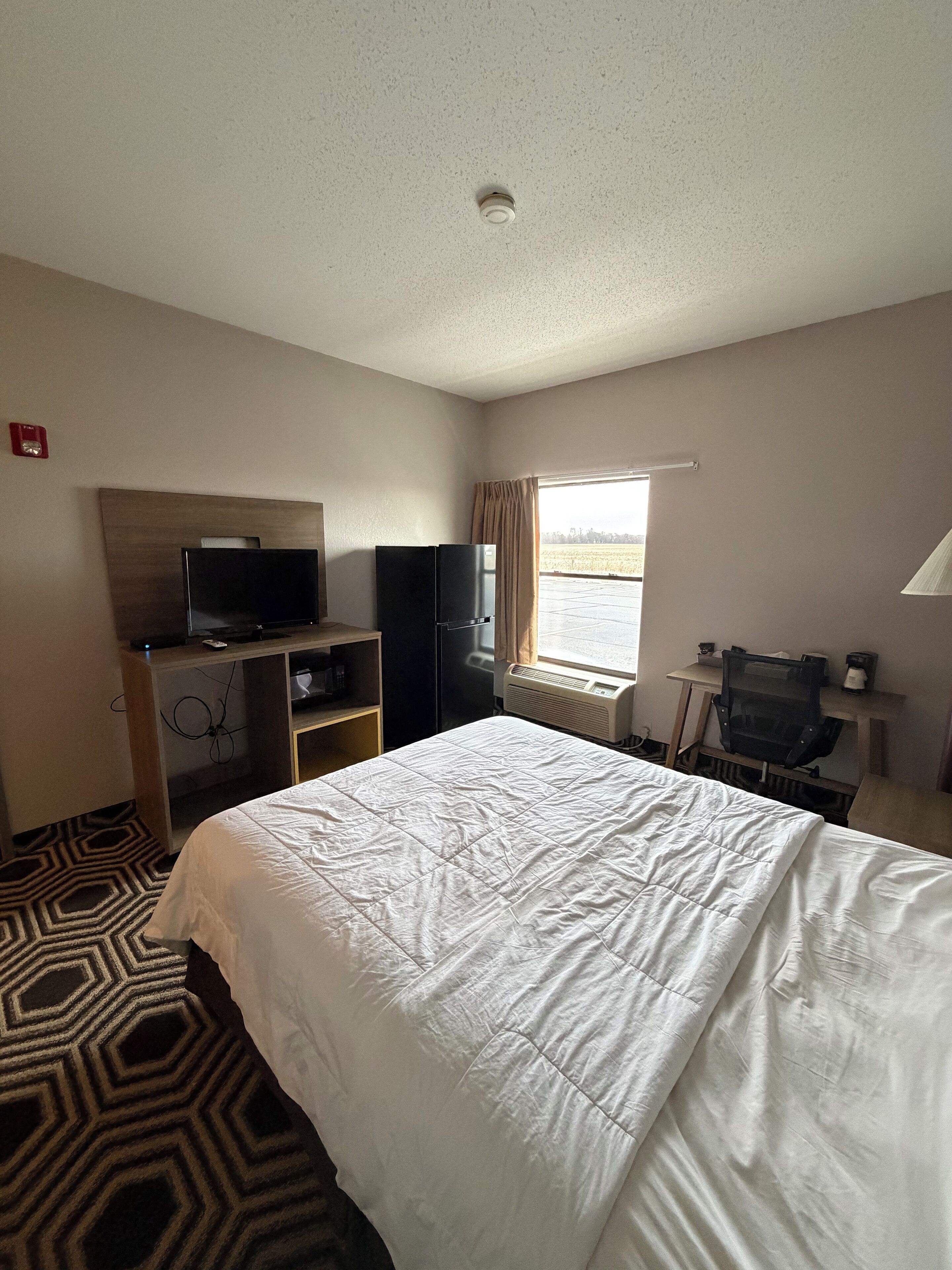 A hotel room with a bed, a television, a desk, and a window with curtains.