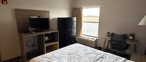 A hotel room with a bed, a television, a desk, and a window with curtains.