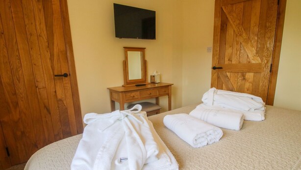 A hotel room with a bed, a wooden dresser, a mirror, and a TV mounted on the wall. - 1 Clarkes Lane (Oswestry)