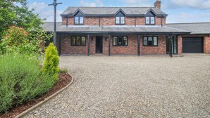 A two-story brick house with a gravel driveway and a black garage door. - 1 Clarkes Lane (Oswestry)