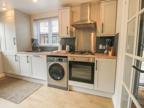 A modern kitchen with a built-in washer, oven, and stove, and a window with blinds. - 1 Clarkes Lane (Oswestry)