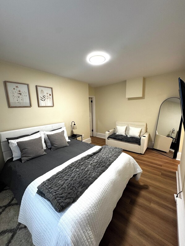 A bedroom with a large bed, a smaller sofa, a mirror, and two framed pictures on the wall. - Charming Trolley Square Stay • Walk to Everything (Wilmington)