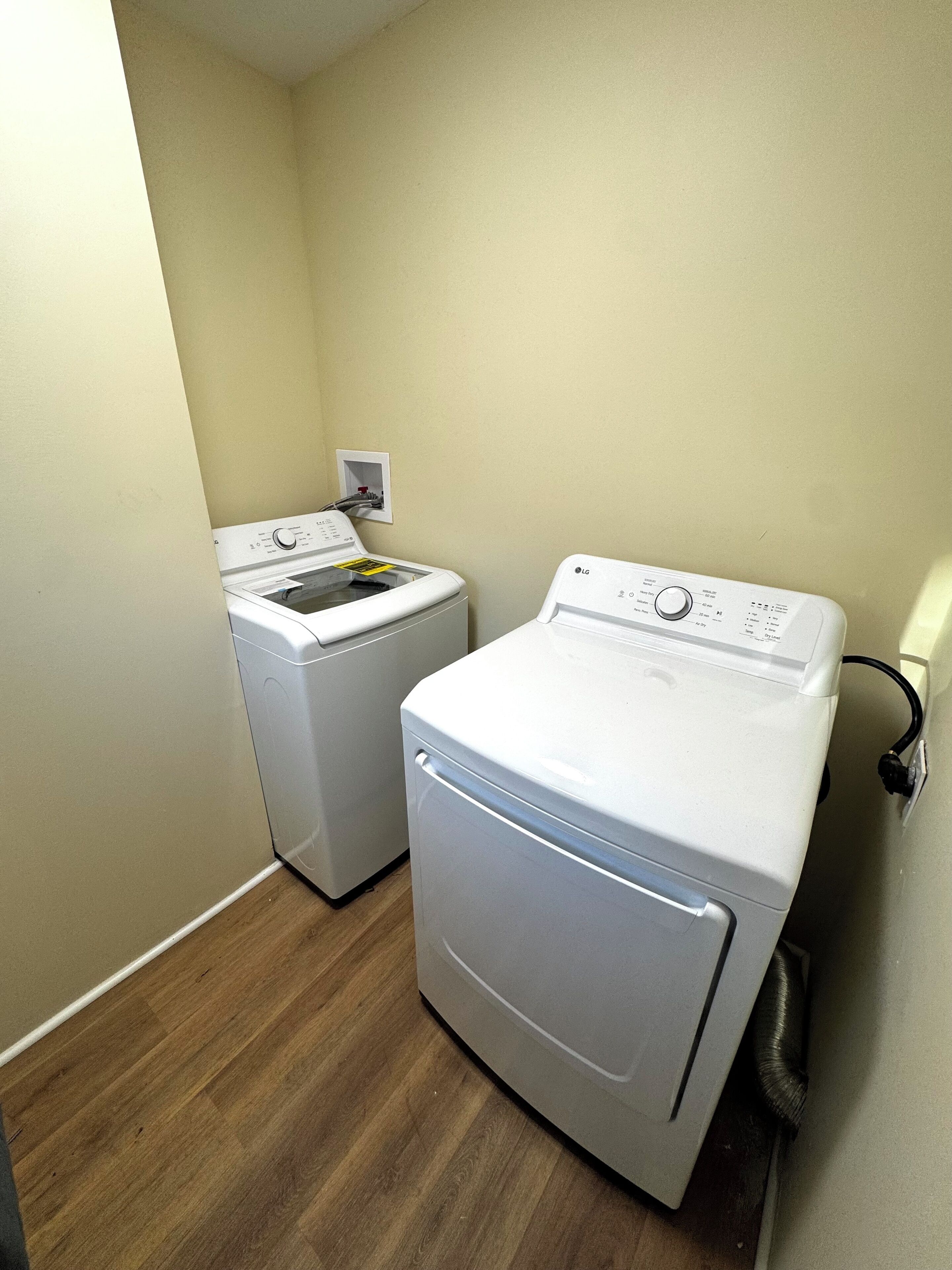 A laundry room with two white front-loading washing machines, wooden flooring, and a light-colored wall.