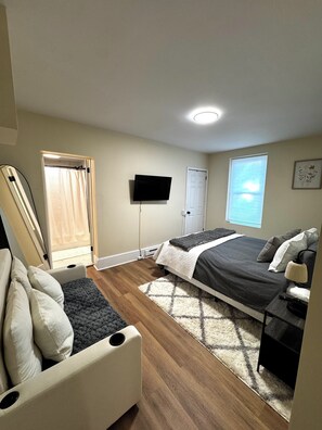 A bedroom with a bed, a TV, a window, and a door.
