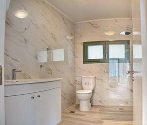 A bathroom with a marble wall, a white sink, a toilet, and a shower enclosure. - Ouzo Stone House1 with Private Pool and Parking (Agios Isidoros)