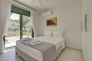 Ein Schlafzimmer mit Bett, weißen Vorhängen, einer Klimaanlage, einem Gemälde und Blick ins Grüne.