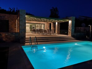 A pool with a clear blue water surface, a covered patio area with outdoor seating, and stone walls. - Ouzo Stone House1 with Private Pool and Parking (Agios Isidoros)