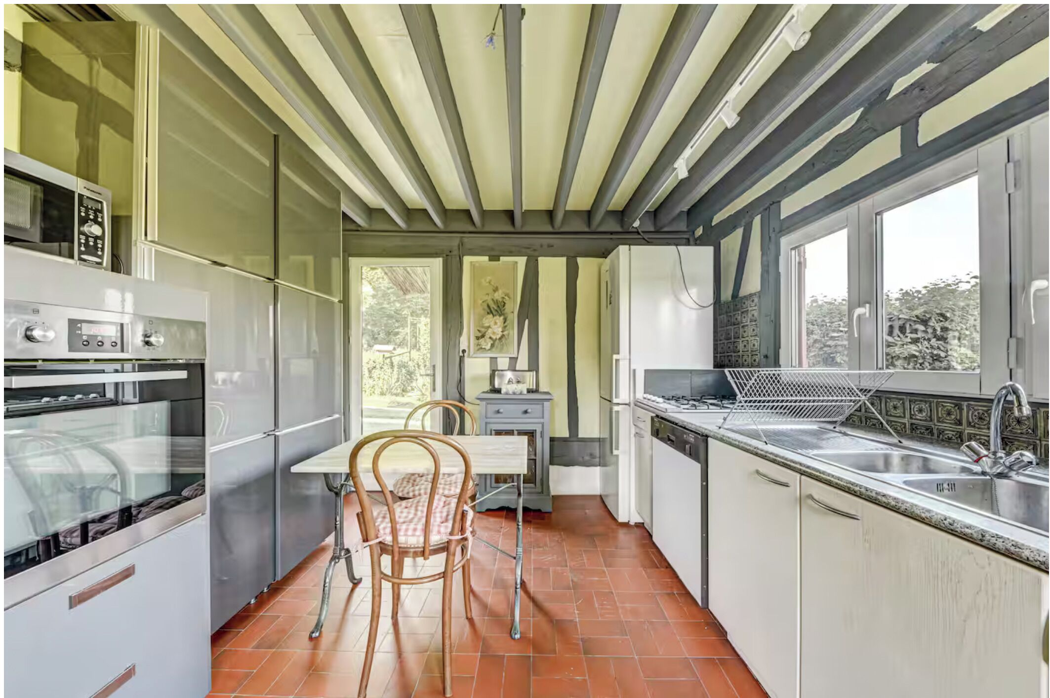 A compact kitchen with modern appliances, a dining area with a table and chairs, and large windows providing natural light.