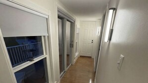 A hallway with a wooden floor, white walls, and a sliding glass door leading to a balcony.