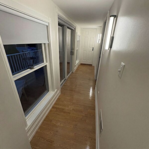 A hallway with a wooden floor, white walls, and a sliding glass door leading to a balcony.