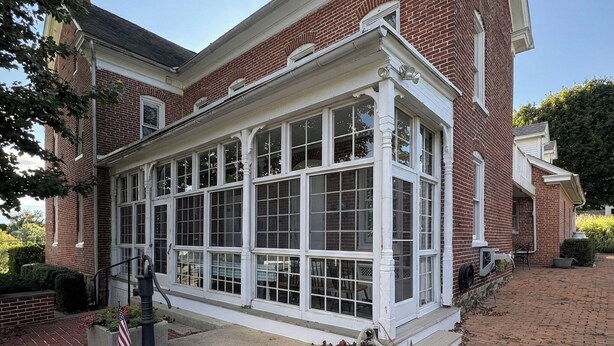 A brick house with a large bay window, a concrete front porch, and a small American flag.