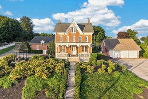 A large brick house with a front porch, surrounded by well-maintained gardens and a clear sky.