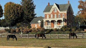 A large brick house with a porch and a fenced field with horses.