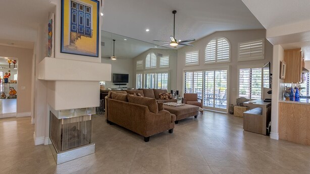 A spacious living room with a fireplace, large windows, and a ceiling fan. - Peaceful 3 bed 2 bath spacious home at Avondale Golf Club Palm Desert (Palm Desert)