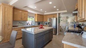 A modern kitchen with wooden cabinets, a large island, stainless steel appliances, and a dining area with a glass table. - Peaceful 3 bed 2 bath spacious home at Avondale Golf Club Palm Desert (Palm Desert)