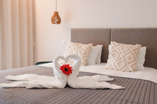 A neatly made bed with a heart-shaped towel arrangement and a red flower centerpiece. - Magnificent 2-bedr. apartment in downtown Olhão, fully equipped with private parking. (Olhão)