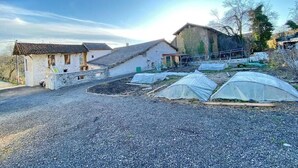A rural property with a gravel driveway, a small building with a tiled roof, and several covered garden beds. - Chalet-style self-contained cottage in quiet countryside (Voiron)