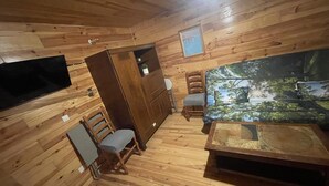 A wooden cabin interior with a sofa, a small table, a TV mounted on the wall, and a wooden cabinet. - Chalet-style self-contained cottage in quiet countryside (Voiron)