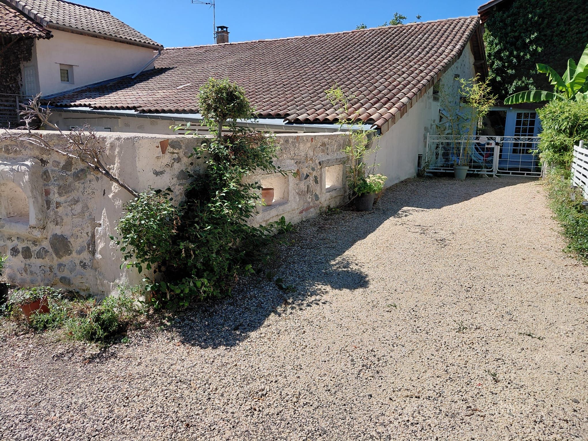 A gravel driveway leading to a building with a tiled roof and stone walls.
