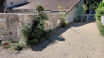 A gravel driveway leading to a building with a tiled roof and stone walls.