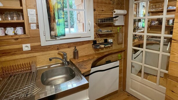 A compact kitchen with wooden walls, a built-in sink, and a window with a view of greenery. - Chalet-style self-contained cottage in quiet countryside (Voiron)