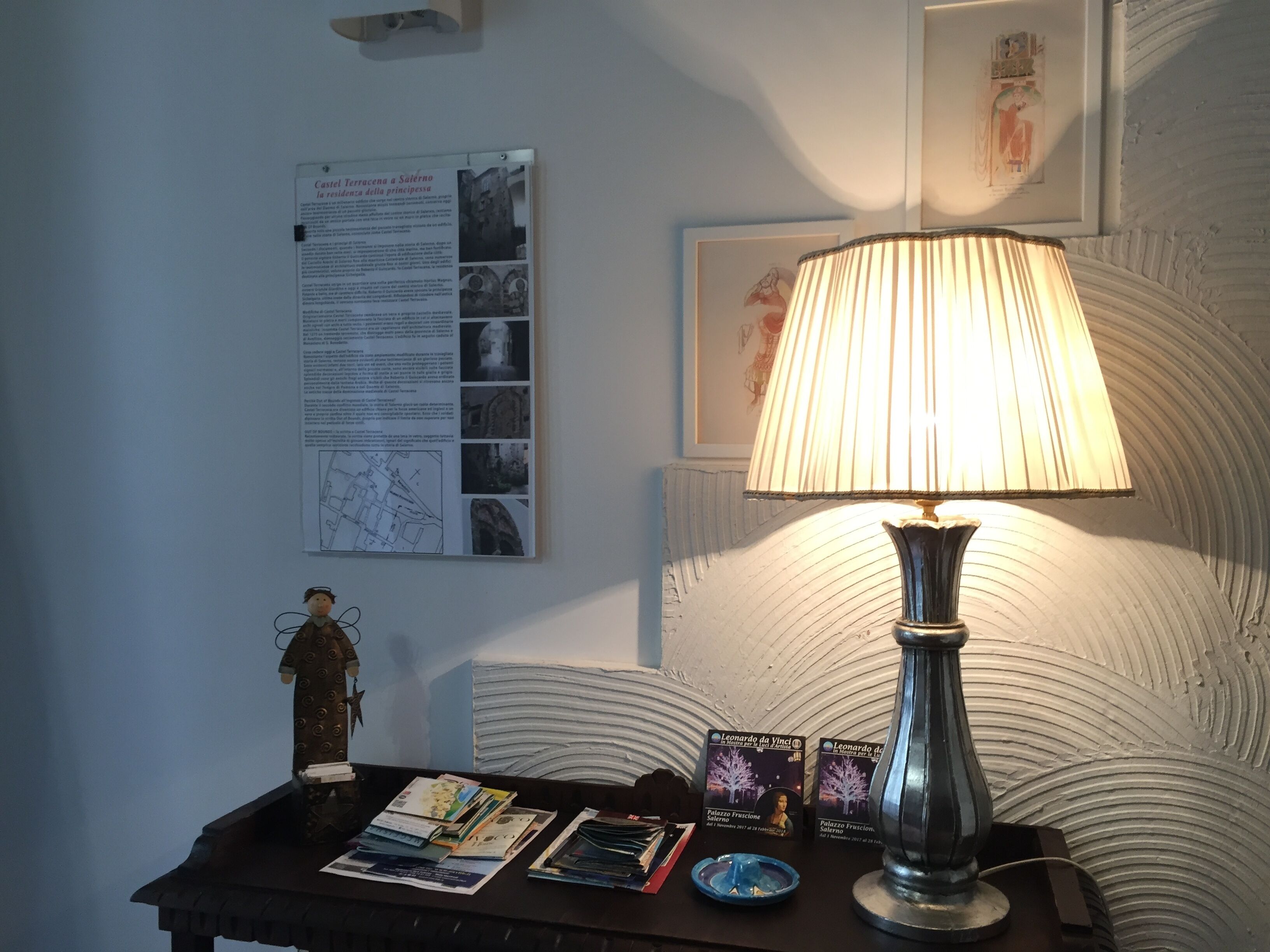 A room with a table displaying informational materials, a lamp, and framed artwork on the wall.