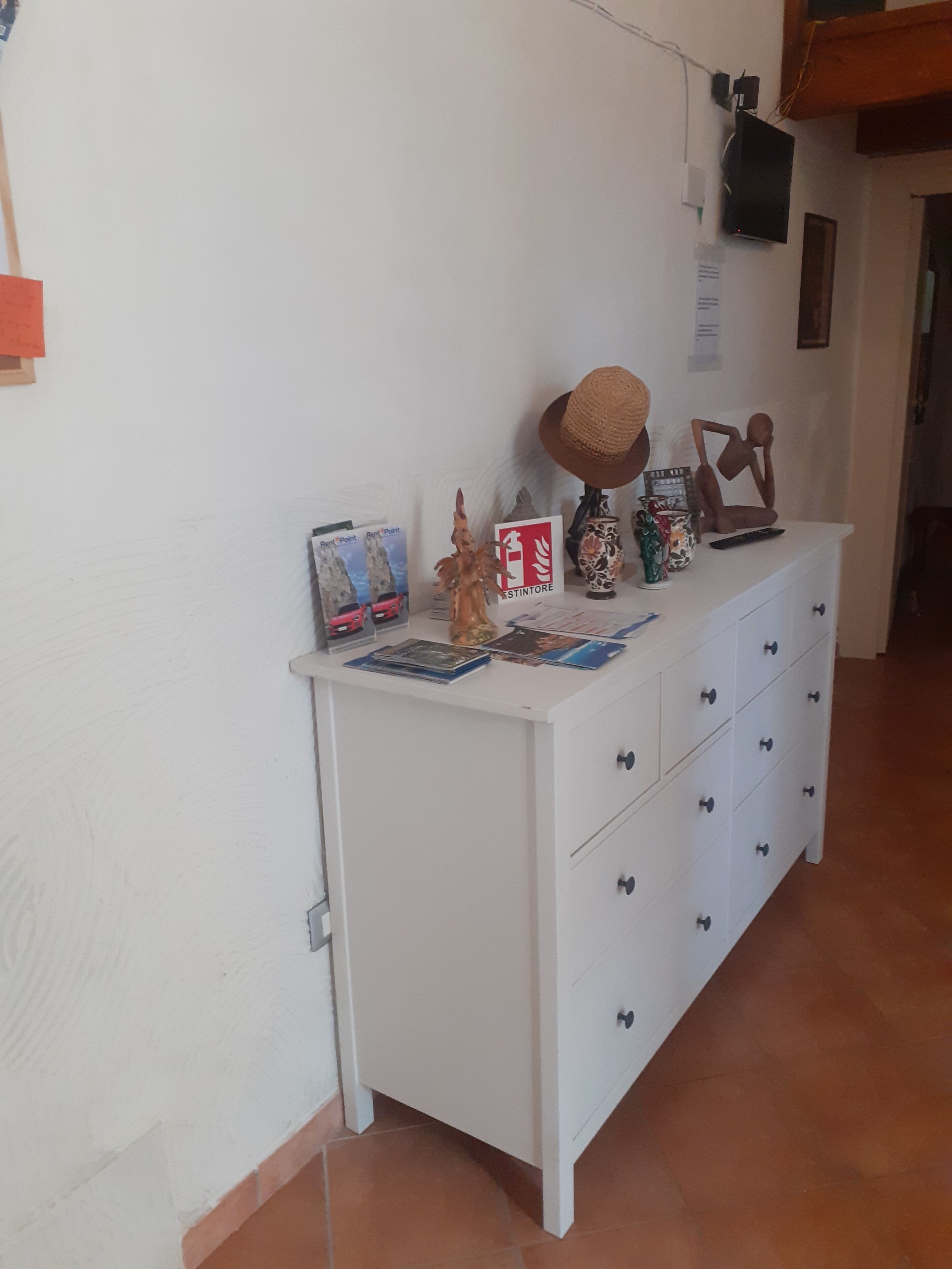 A white dresser with multiple drawers and a shelf, placed against a wall with a tiled floor.