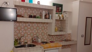 A compact kitchen with white cabinets, a built-in oven, and a small sink. There is a TV mounted on the wall above the counter. - casa normanna (Salerno)