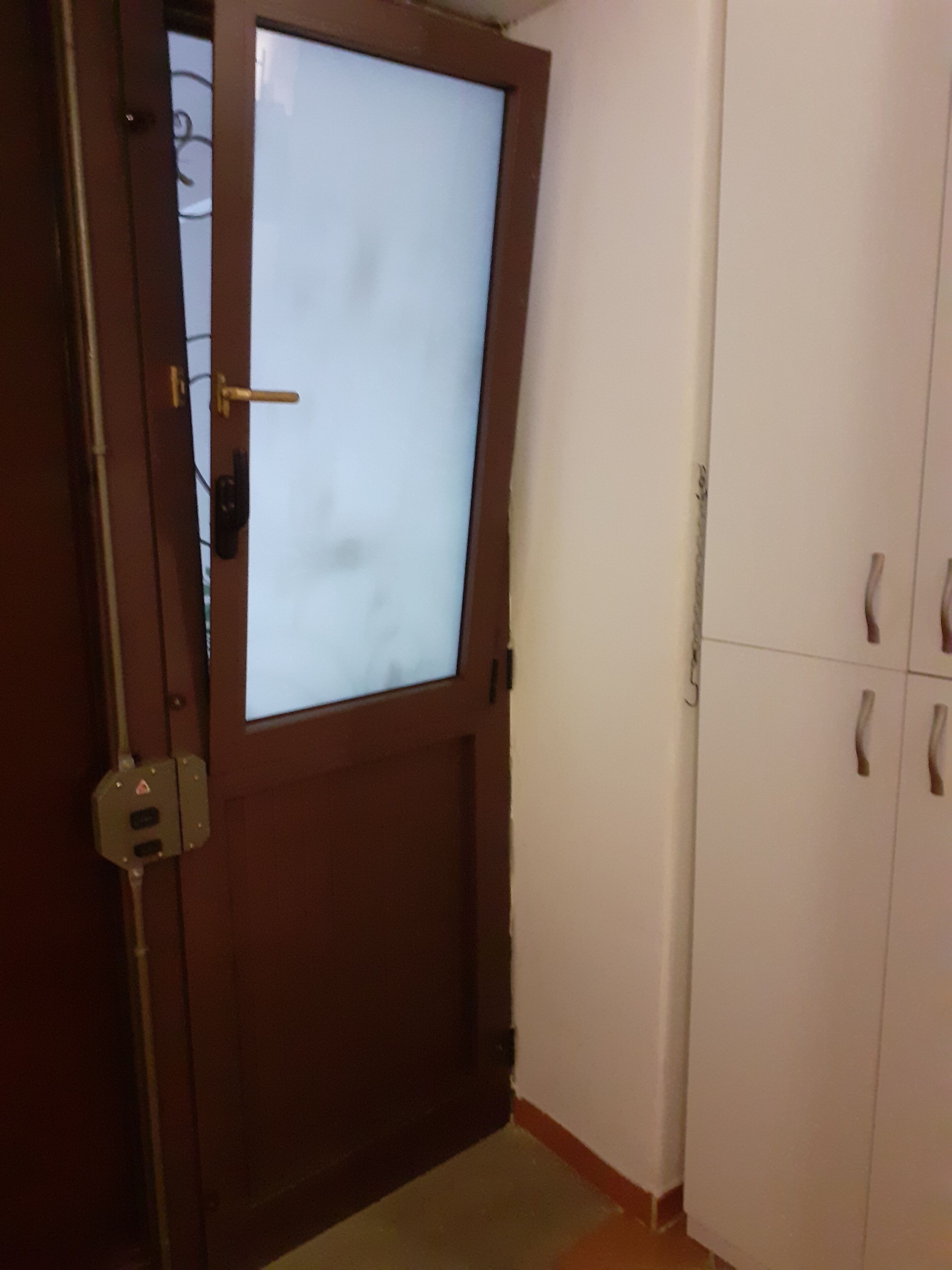 Una porta in legno con un pannello di vetro satinato, una parete bianca e un armadio bianco con due ante e due cassetti.